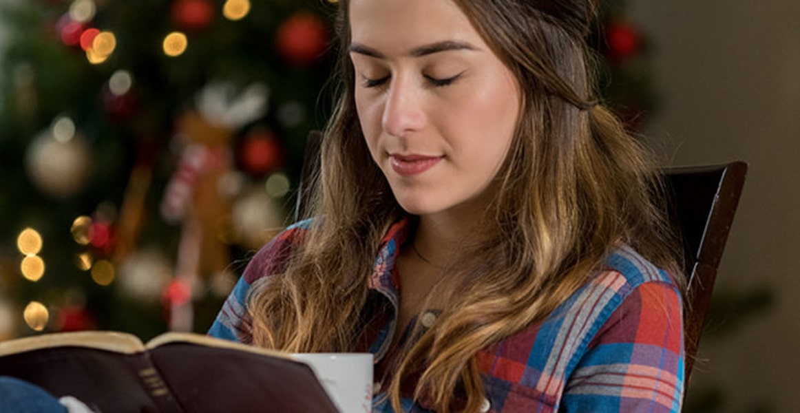 Femme assise devant un sapin de Noël avec un livre à la main et les yeux fermés