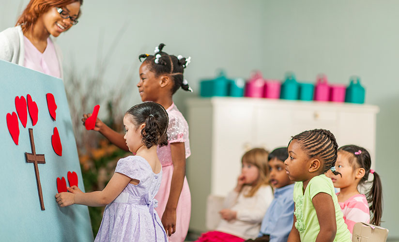 A sunday school teacher guides kids as they help decorate a felt poster