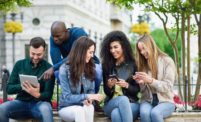 A group of young adults seated outside while scrolling on their phones