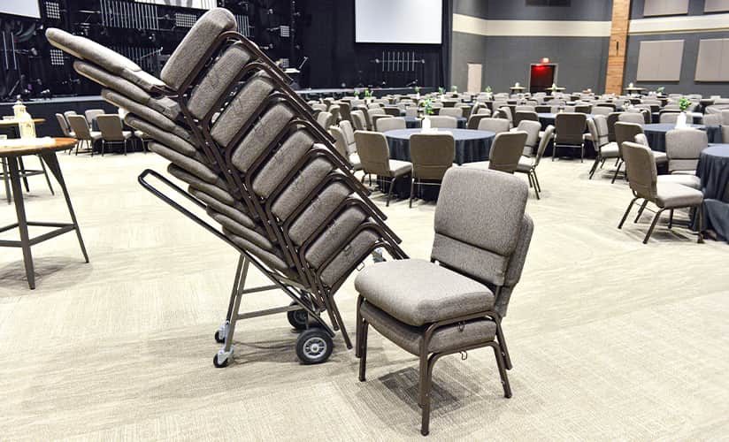 Chaises Bertolini empilées sur un chariot dans une grande salle d'église