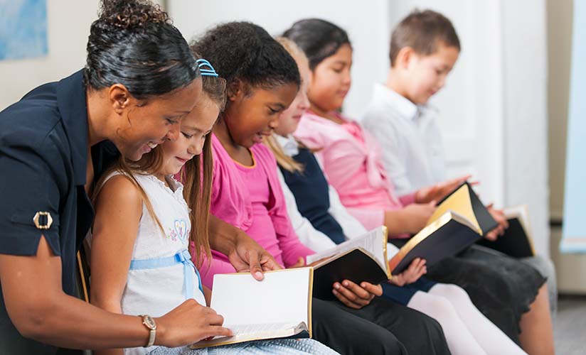 Professora e crianças em uma aula da Escola Dominical lendo e cantando juntos