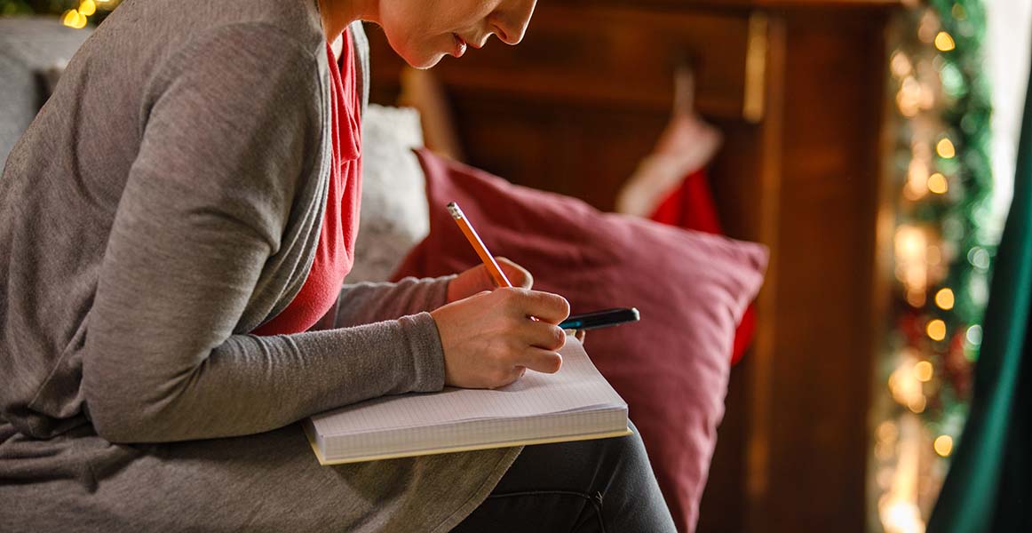 Una mujer en un entorno con temática navideña, escribiendo en un cuaderno.