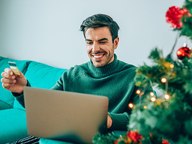 uomo seduto al computer, che pianifica e fa shopping, circondato da decorazioni natalizie