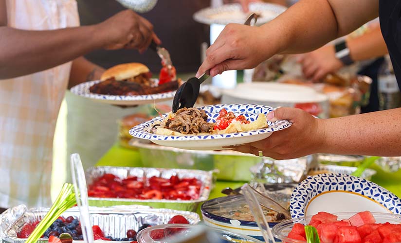 Close up of a potluck table and people filling their plates