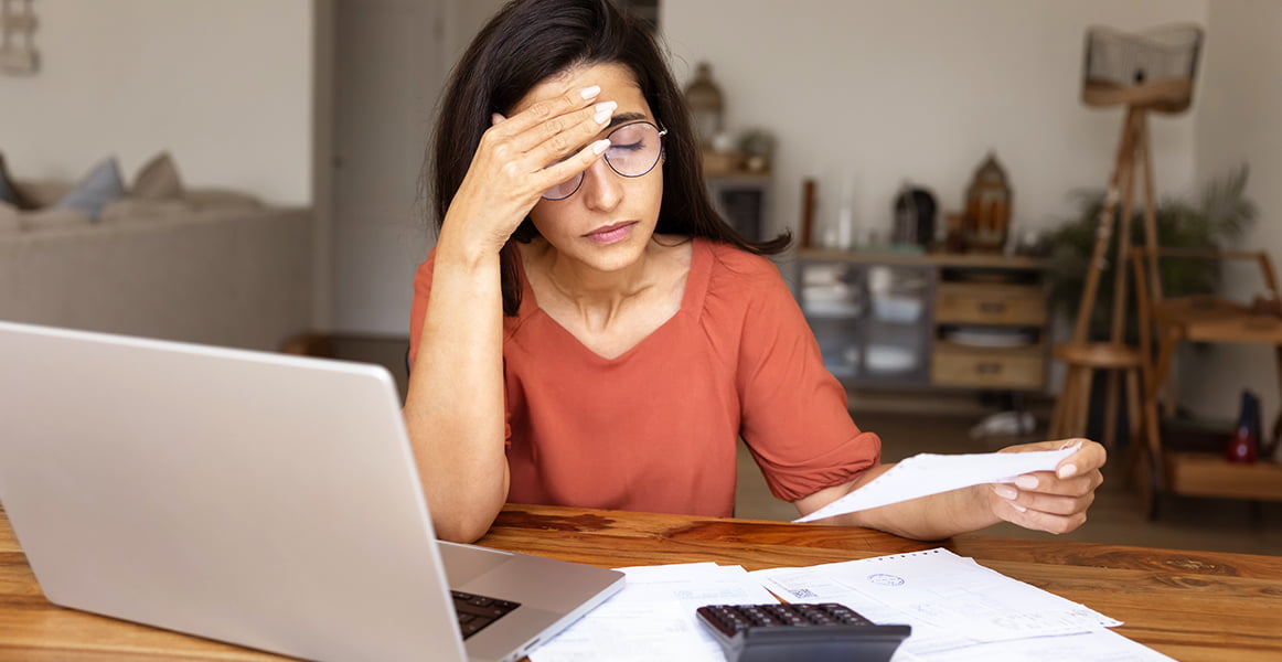 A stressed woman sitting at a computer with papers scattered on her desk