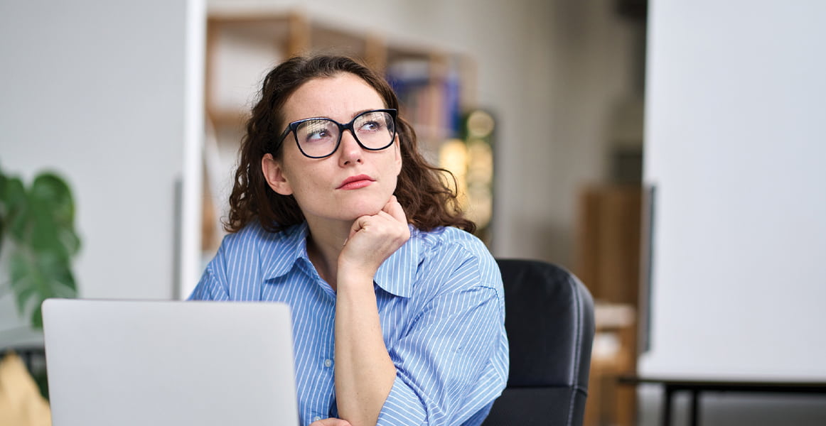Eine Frau, die an ihrem Laptop arbeitet und nachdenklich wegschaut.
